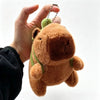 A hand holds a brown capybara plush toy with green accents, featuring a mama and four babies.