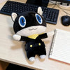 A black and white plush doll of Persona 5 Morgana sitting on a wooden desk next to a notebook and computer equipment.