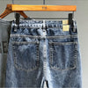 A pair of dark blue vintage loose fit denim harem jeans with visible pockets and a wooden hanger.