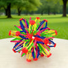 A colorful, expandable magic ball toy with multiple streamers in red, yellow, green, and blue resting on a white surface.