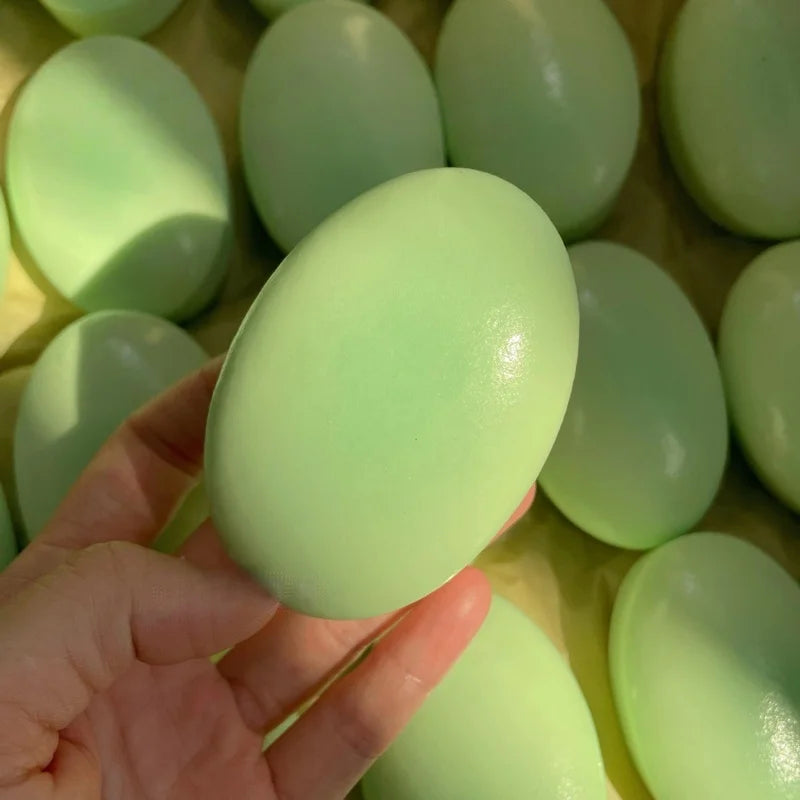 A hand holds a light green, cheese-shaped squishy stress relief toy against a background of similar toys.