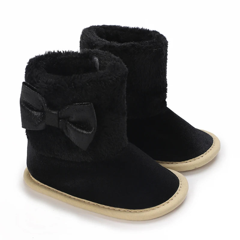 A pair of black faux fur baby first walker shoes with a bow detail.