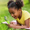 A young girl is holding a green handheld insect catcher outdoors on the grass.