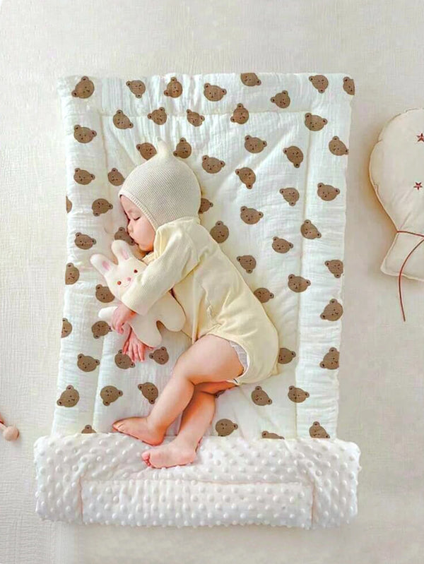 Un bébé portant un bonnet en polaire beige et une tenue jaune, allongé sur une couverture blanche à motifs d'ours marrons.
