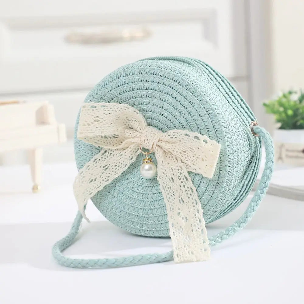 A light mint green handwoven straw crossbody bag with a cream lace bow and strap.