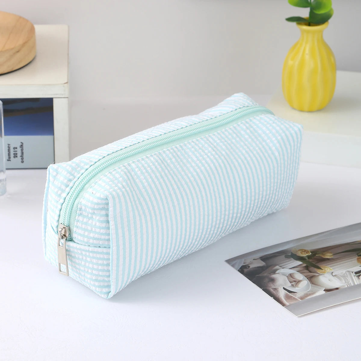 A light blue and white striped canvas pencil case with a zipper is displayed on a white surface.