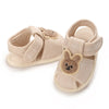 Pair of light beige soft sole sandals for baby's first steps featuring a cute bear design