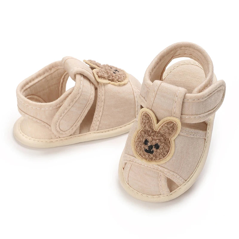 Pair of light beige soft sole sandals for baby's first steps featuring a cute bear design