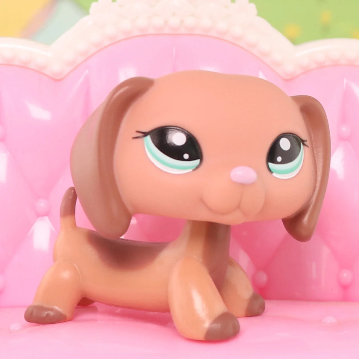 A small, light brown miniature pet animal figure with large eyes is displayed in a pink decorative setting.