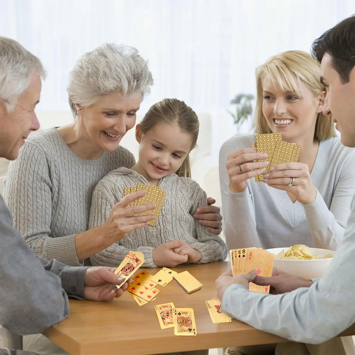 Three people are playing with a deck of golden waterproof playing cards indoors.