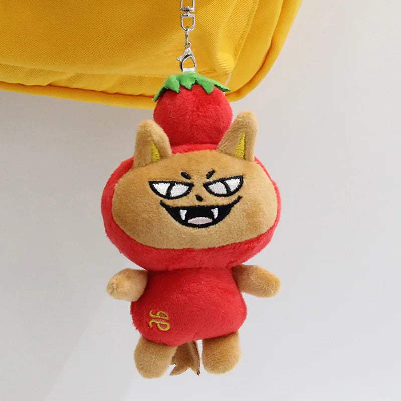 A plush pendant doll of a red, angry-looking creature with green leaves hanging from a yellow fabric.