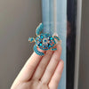 A close-up of a sparkling blue rhinestone turtle brooch pin being held by a hand.