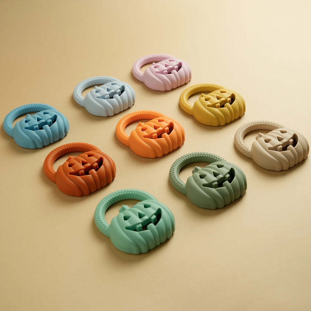 A collection of silicone pumpkin baby teethers in various pastel colors, including pink, blue, yellow, orange, and green.
