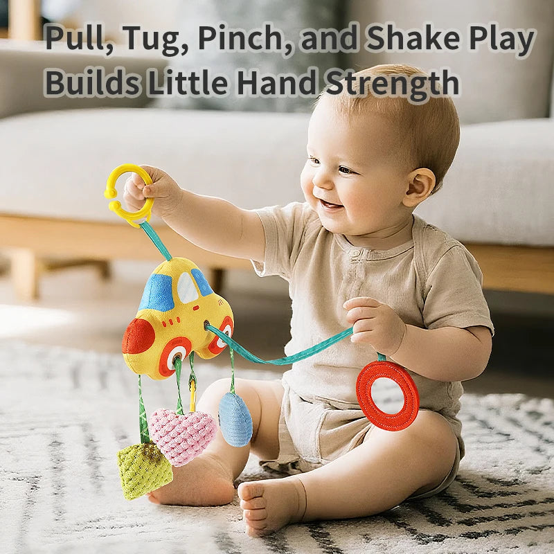 A baby is playing with a yellow crab-themed rattle and teether toy with hanging straps on a rug.