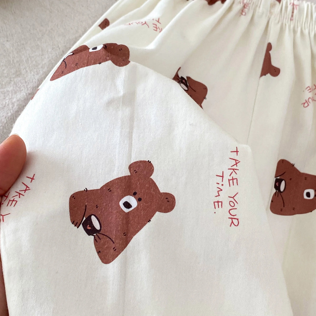 Close-up of white casual pants featuring brown bear print details and elastic waistline.