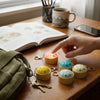 A hand is holding a yellow dumpling squishy keychain with an LED glow on a wooden table.
