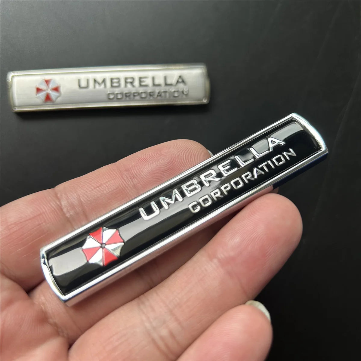 A silver and black emblem badge for Umbrella Corporation, featuring a red and white cross design.