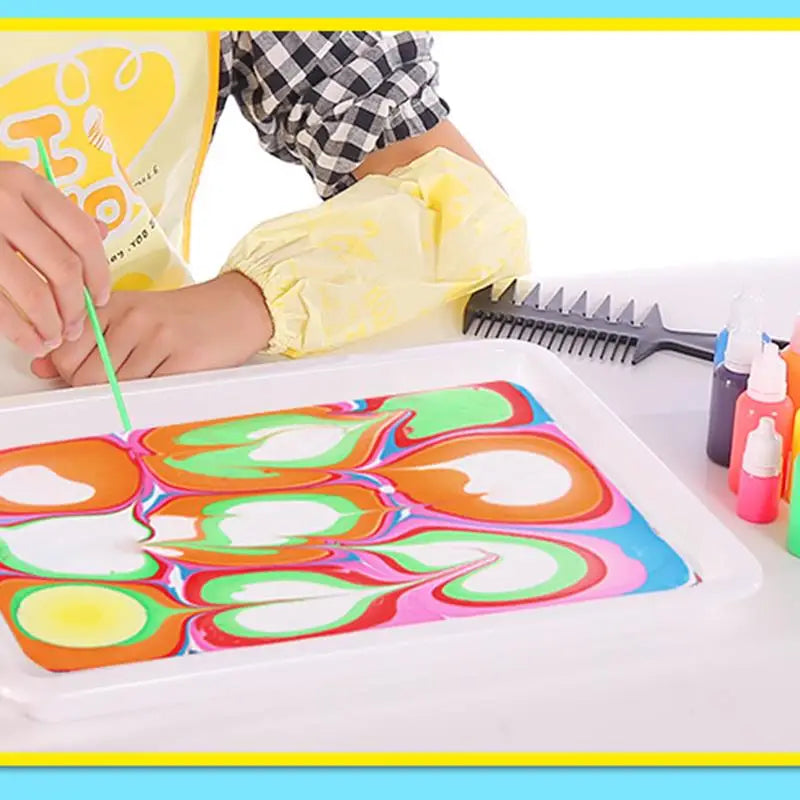 A child is using a paintbrush to apply colorful water marbling paint onto a silicone tray.