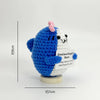 A handwoven crochet ornament depicting a blue shark with a pink fin and a white shark, used as desk decor.