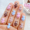 A hand displays various mini resin teddy bear charms in pink, purple, and blue colors for DIY crafts.