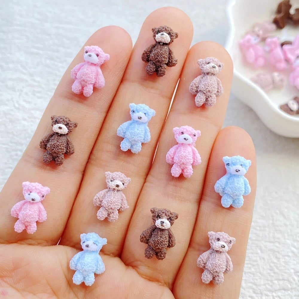 A hand displays various mini resin teddy bear charms in pink, purple, and blue colors for DIY crafts.