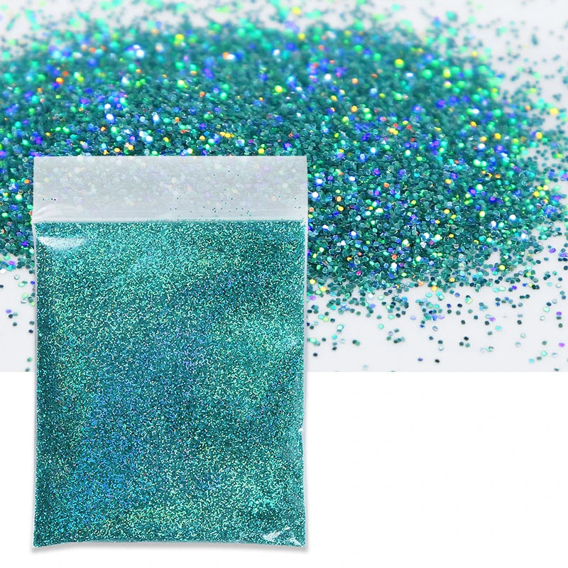 A small white bag filled with vibrant teal holographic glitter powder next to a loose pile of the same glitter.