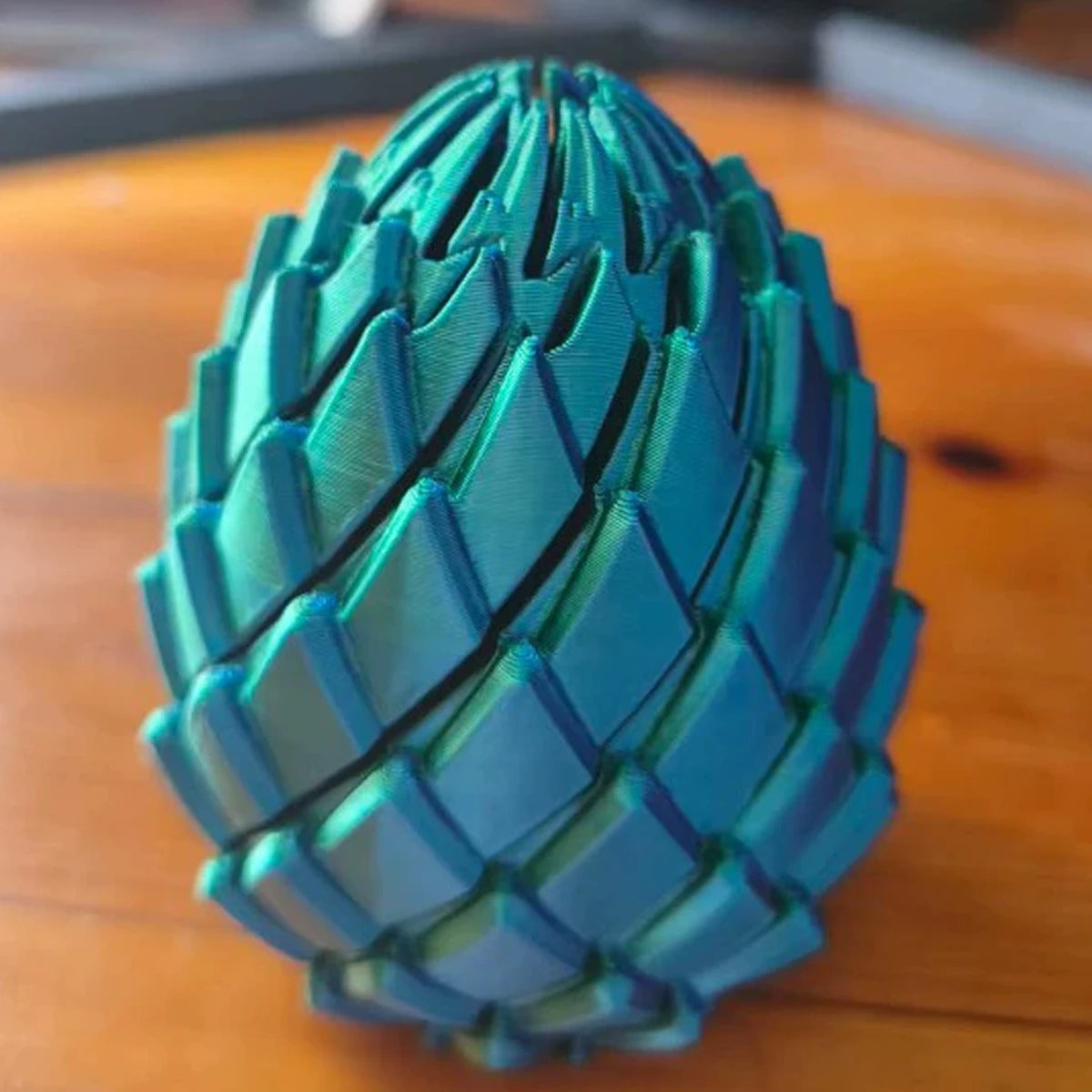A teal 3D printed expandable dragon egg fidget toy resting on a wooden surface.