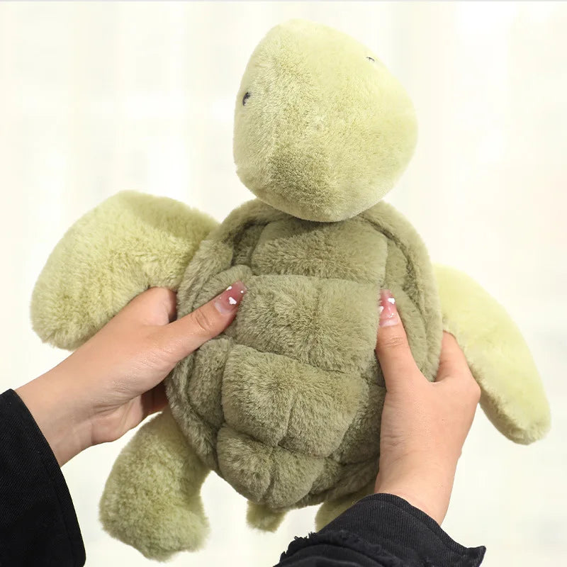 A person is holding a soft, light green simulated turtle plush doll.
