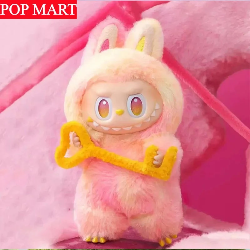 A fluffy pink Labubu plush doll with yellow accents, featured in a soft pink background.