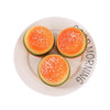 A bright orange squishy hamburger stress ball with white sprinkles is displayed on a white plate.
