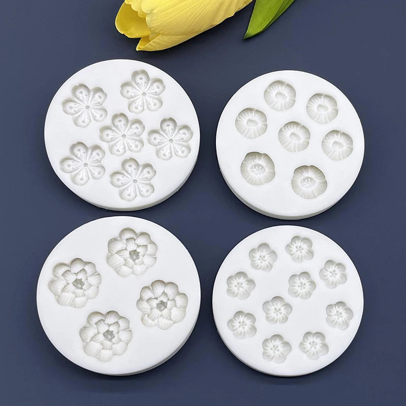 A set of white silicone daisy flower molds for fondant and cake decorating, with a yellow flower petal visible in the backgro