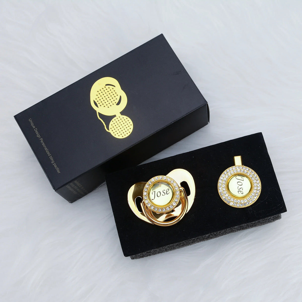 A black box containing a personalized crystal pacifier and clip gift set with gold accents.