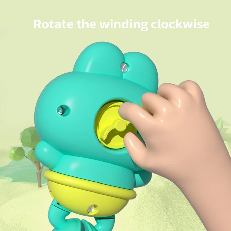 A hand rotates the winding mechanism of a teal floating frog bath toy.