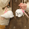A white seal plush toy with pink accents is being held by a person against a brown fabric background.