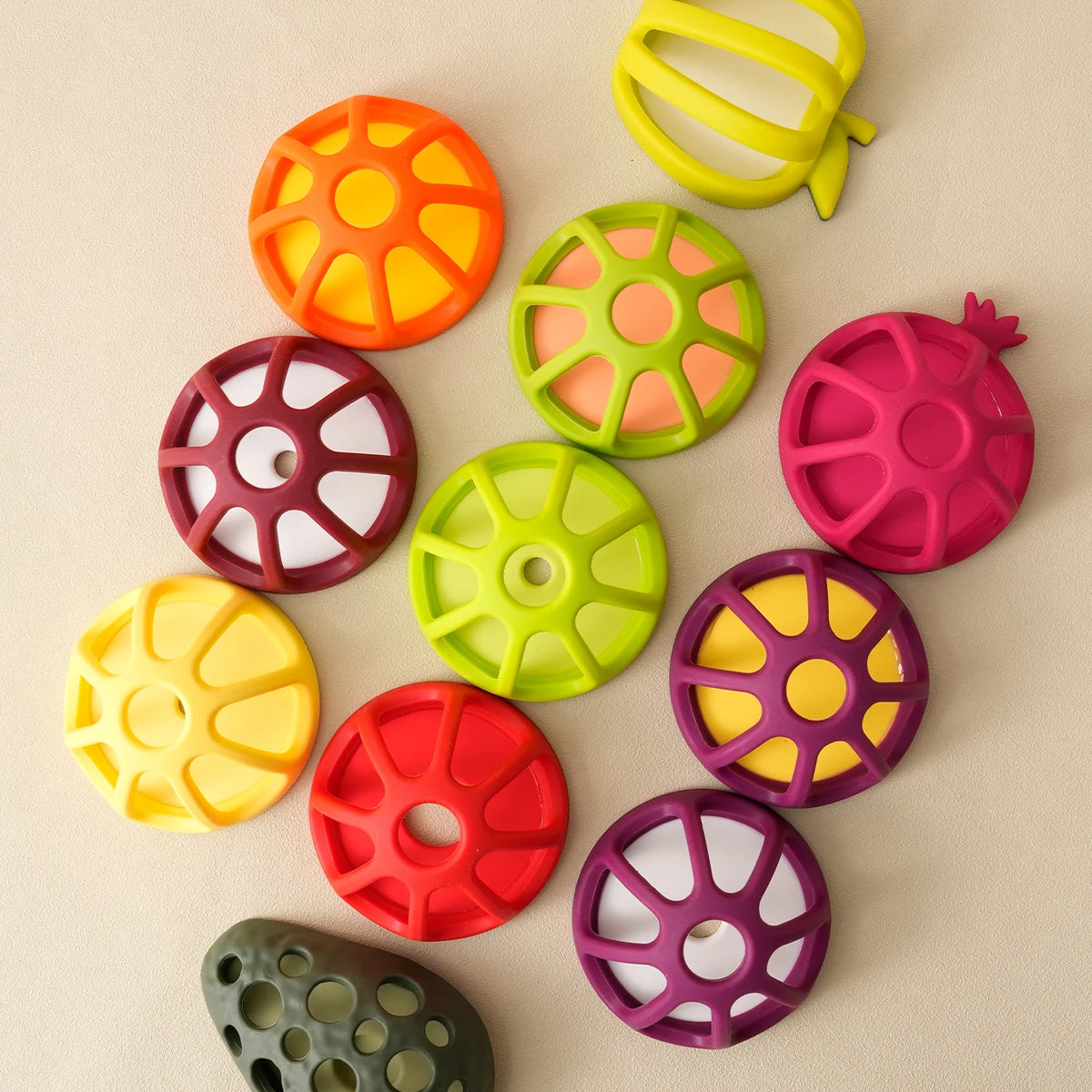 A collection of colorful silicone baby teethers shaped like various fruits and vegetables, including orange, green, pink, yel