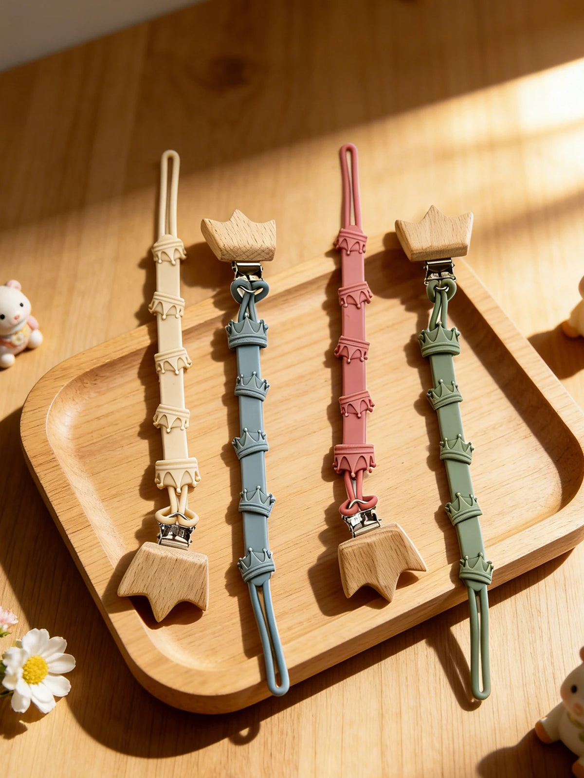 A set of baby pacifier clips featuring burlap flower designs in pastel colors on a wooden tray.