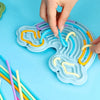 A hand is placing colored silicone strings into the grooves of a light blue sensory activity board.