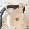 A cream-colored quilted baby diaper caddy organizer is shown with black stroller straps.