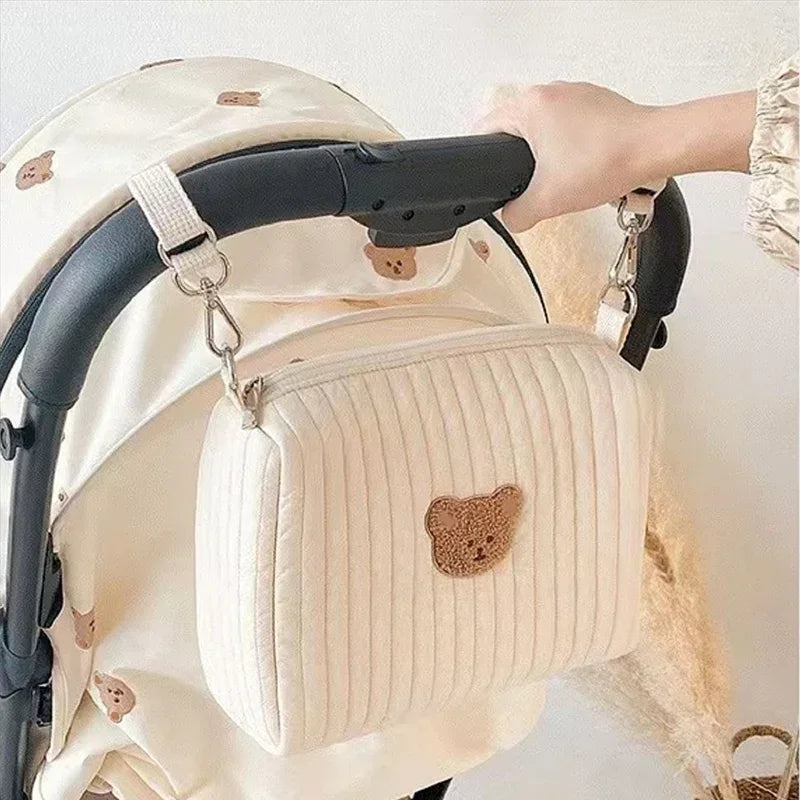 A cream-colored quilted baby diaper caddy organizer is shown with black stroller straps.