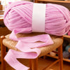 A pink ball of soft chunky t-shirt yarn is displayed on a wooden stool.