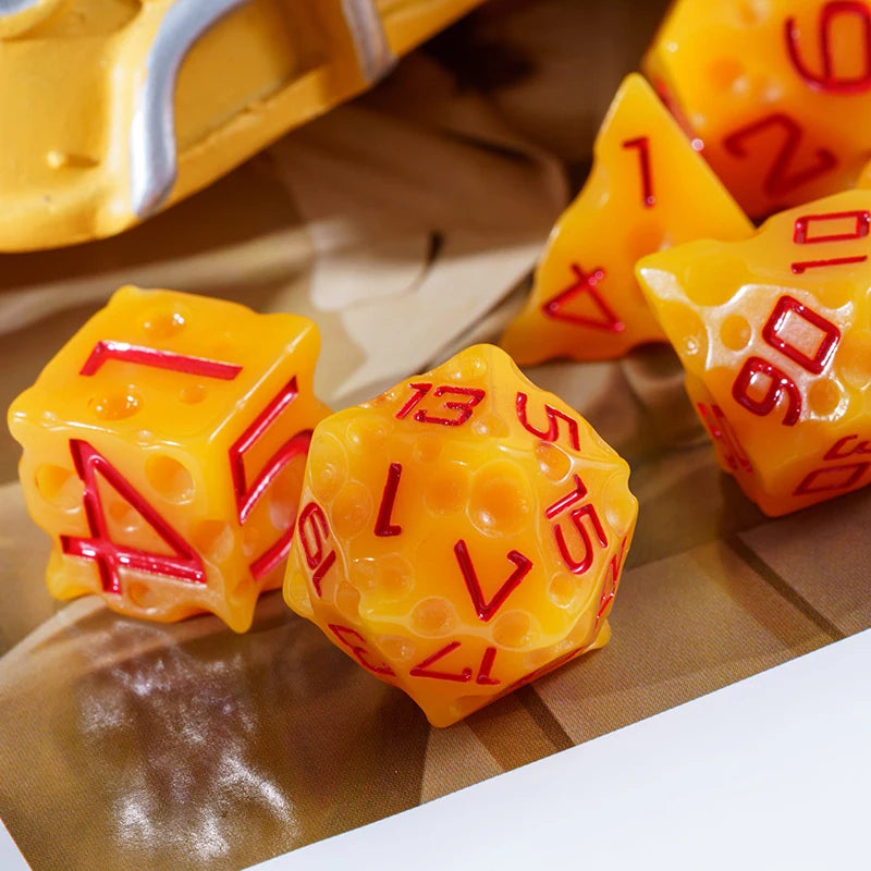 A set of seven yellow cheese-themed polyhedral dice resting on brown parchment paper.