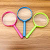 Three plastic magnifying glasses in pink, blue, and lime green resting on a wooden surface.