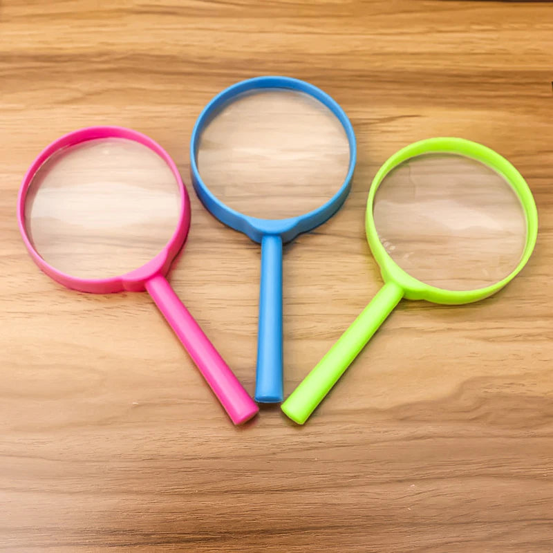 Three plastic magnifying glasses in pink, blue, and lime green resting on a wooden surface.
