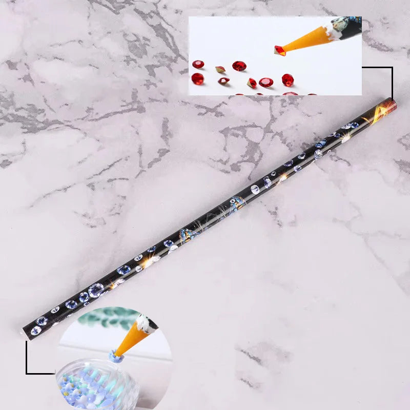 A long, slender pen with a decorative body is shown next to loose red and gold rhinestones and a glass of glitter.