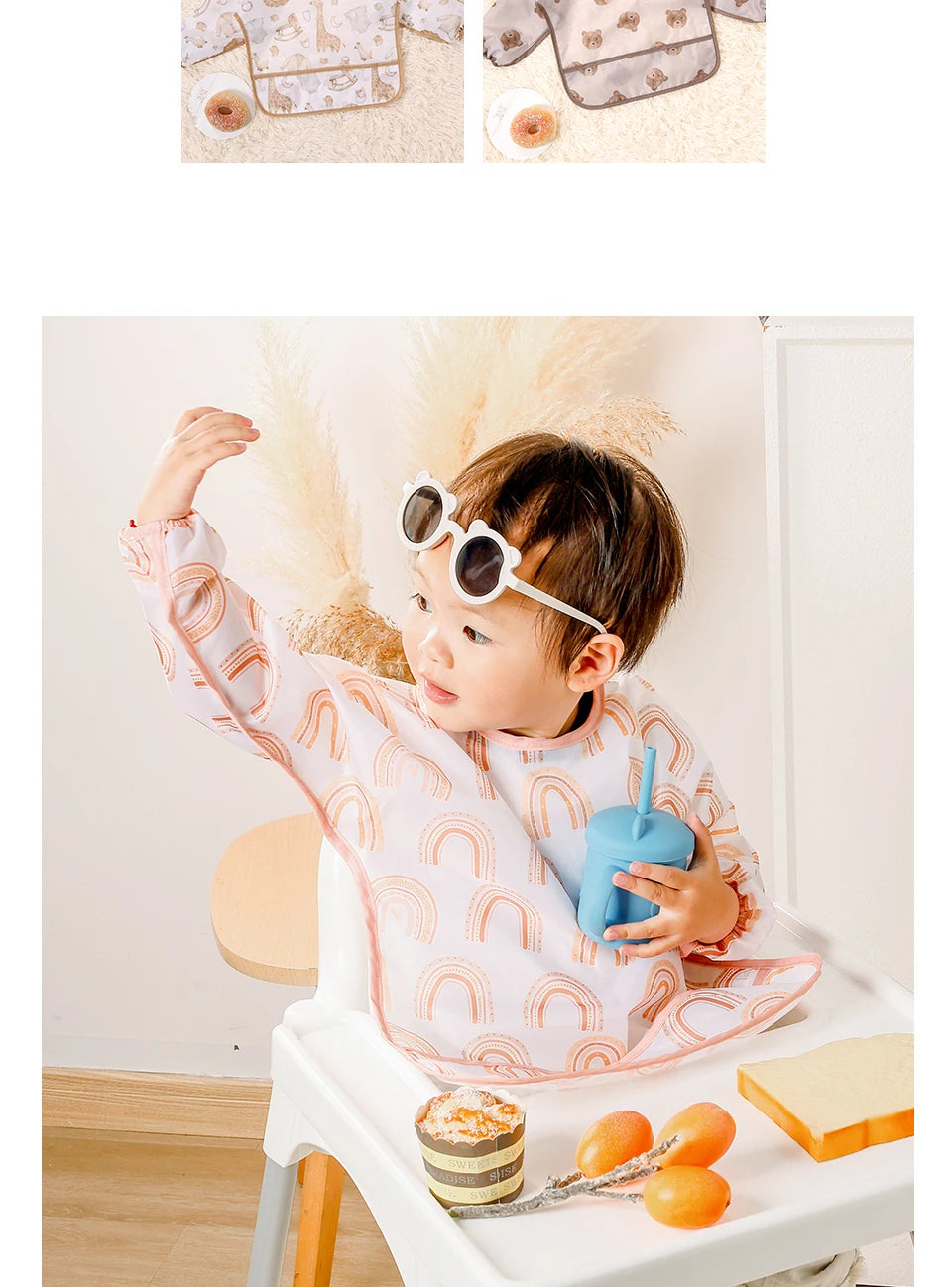 A baby is wearing a pink and white patterned waterproof long sleeve feeding bib while sitting at a table.