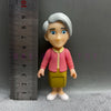 A playful cartoon PVC figurine of a child with white hair and pink clothing standing next to a ruler.