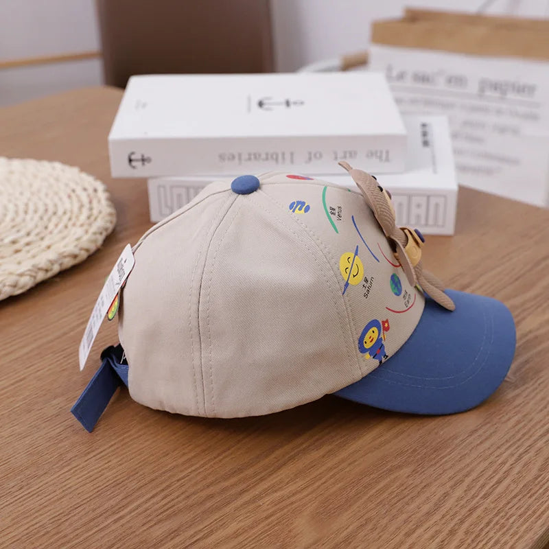 A beige toddler baseball cap with a blue brim and an adjustable strap, featuring colorful bear graphics.