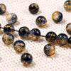 A collection of dark glass beads with a golden crackle finish scattered on a white surface.