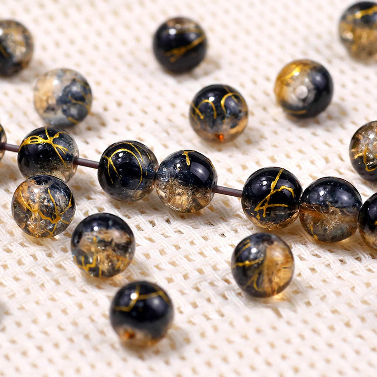 A collection of dark glass beads with a golden crackle finish scattered on a white surface.