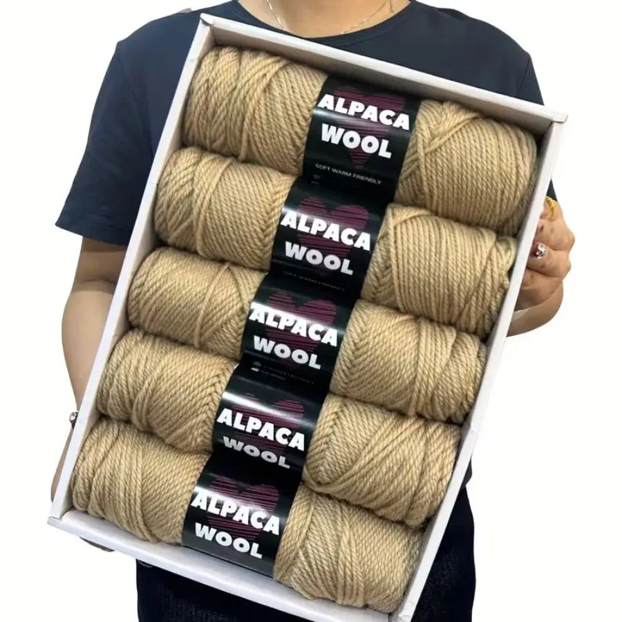 A box containing five skeins of natural beige alpaca wool yarn for knitting and crochet projects.